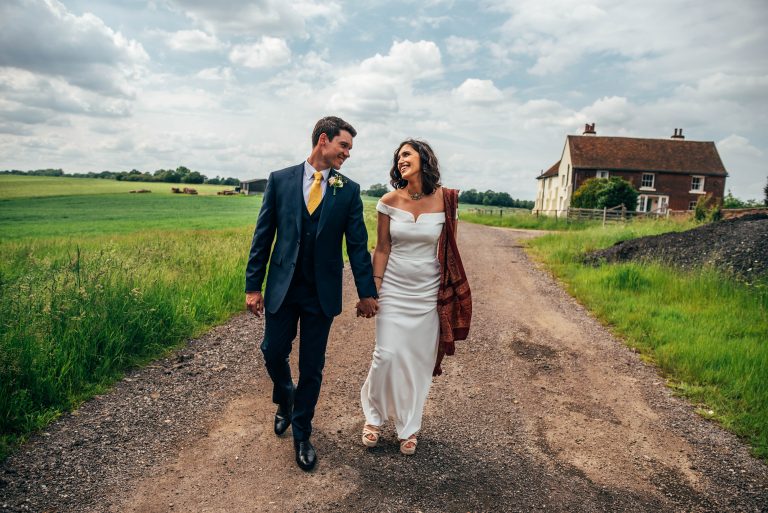 bride and groom walk in field at The Barns at Lodge Farm