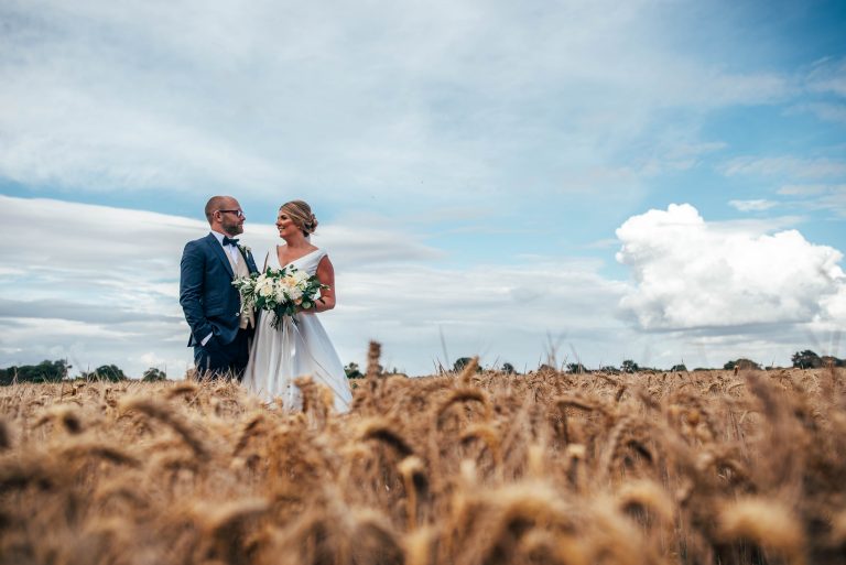 Bride and groom stand together in wheat field at Vaulty Manor