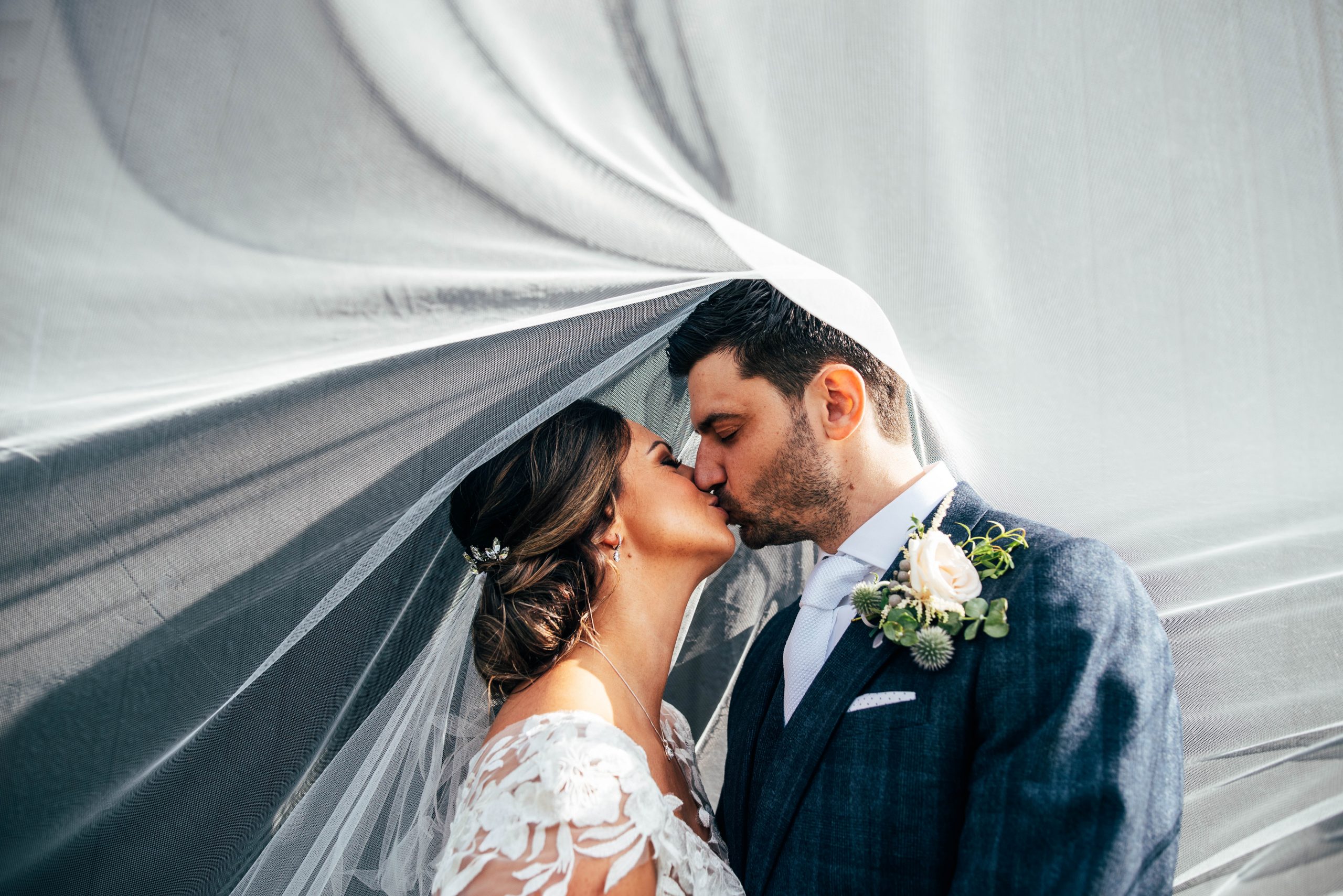 bride and groom kiss under billowing veil