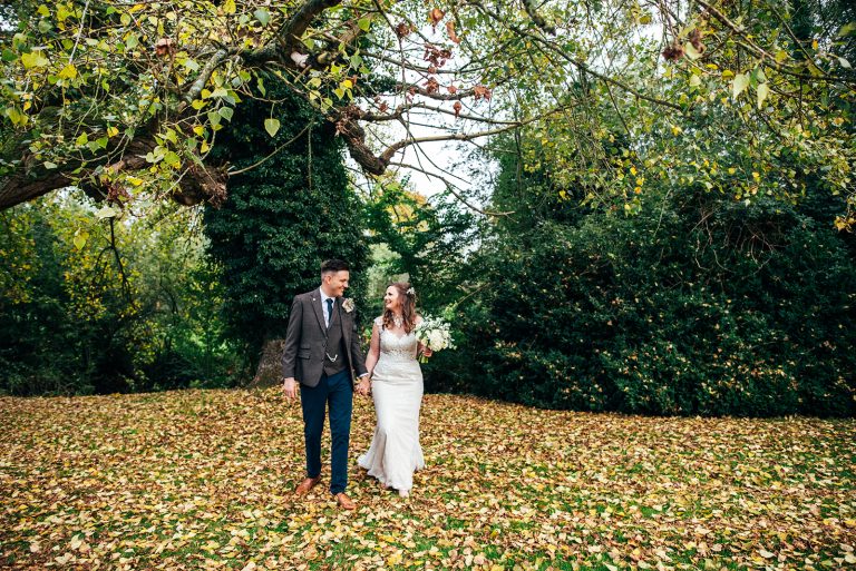 Bride and groom walk in autumn leave at The White Hart Great Yeldham