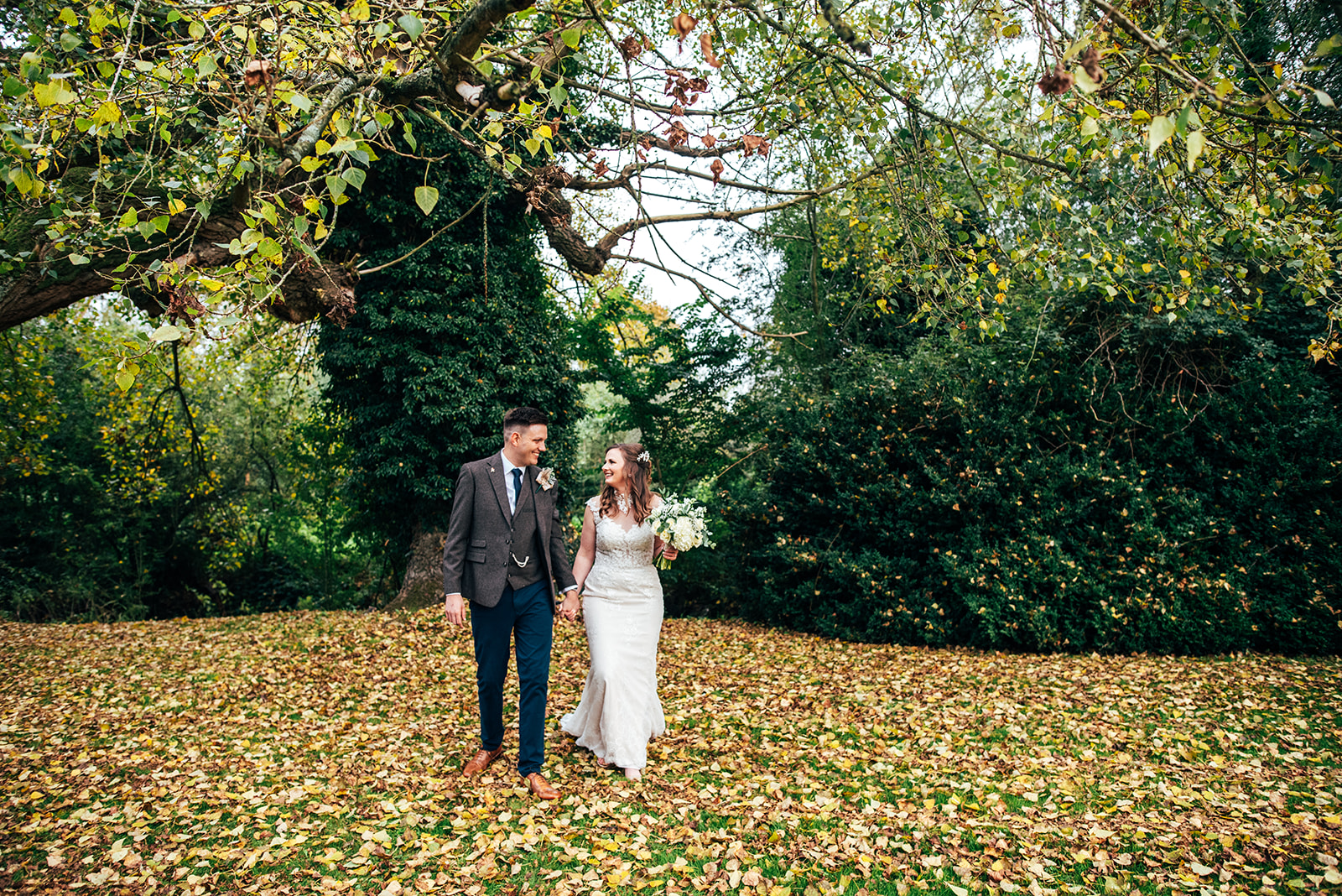 Bride and groom walk in autumn leave at The White Hart Great Yeldham