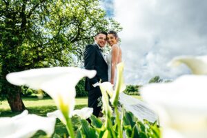Bride and Groom laugh with Lillies in foreground at Villiers Barn. Best Essex documentary wedding photographer