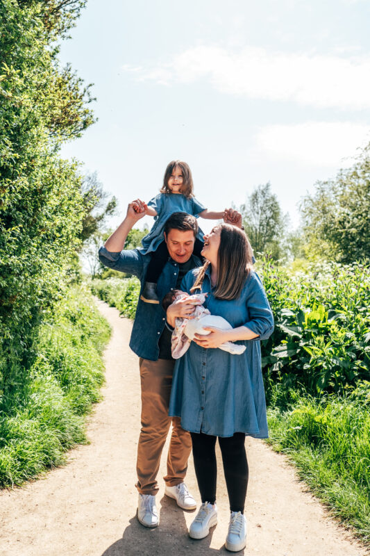 Family of four stand and laugh on path Essex family lifestyle childhood baby photographer