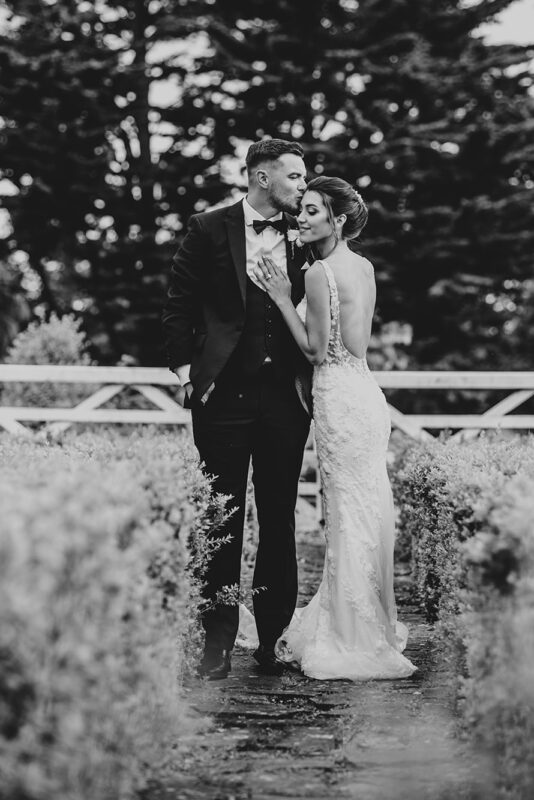 Black and white of bride with groom in black tie kiss in front of a gate at Villiers Barn Best Essex documentary wedding photographer