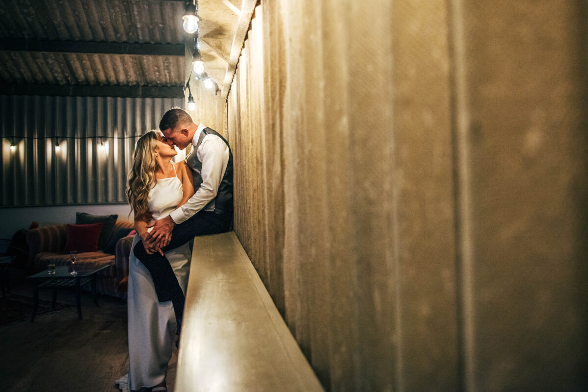 Bride and Groom kiss under festoon lights in barn at Houchins Best Essex documentary wedding photographer