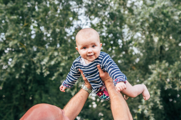 Dad holds baby girl in striped dress up as she smiles to the camera Essex lifestyle family baby childhood photographer