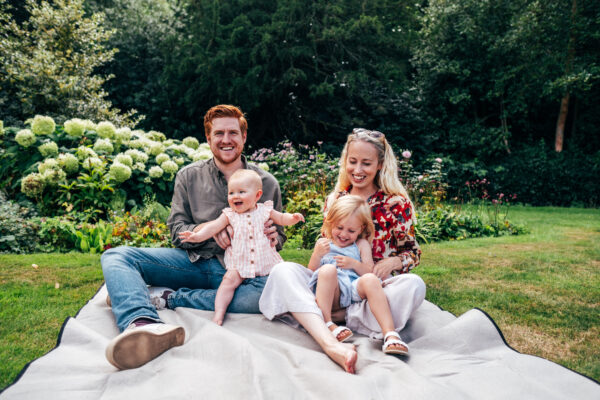 family of four sit on blanket in park and laugh Essex family lifestyle childhood baby photographer