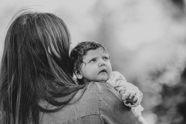 black and white of baby girl looking over her mums shoulder Essex lifestyle family baby childhood photographer