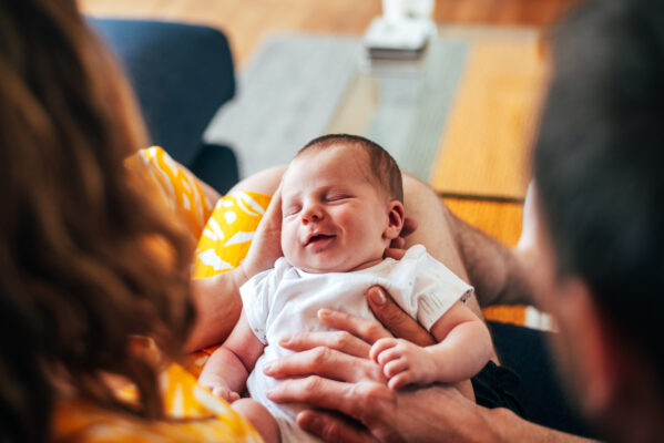 new baby smiles as he lays on parents laps at home Essex newborn baby childhood portrait family photographer