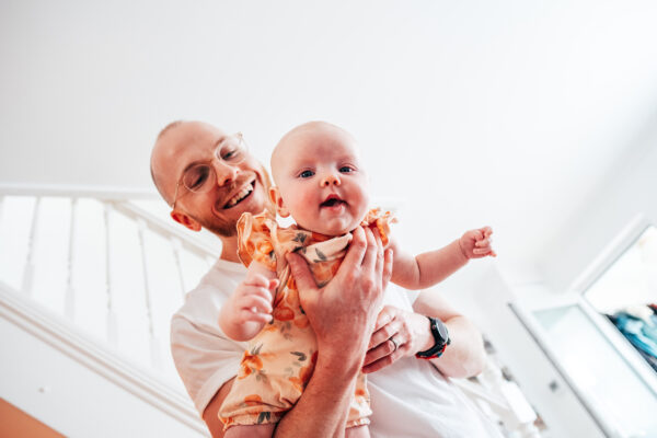 Dad holds his baby girl in the air as she smiles down at camera Essex lifestyle family childhood baby photographer