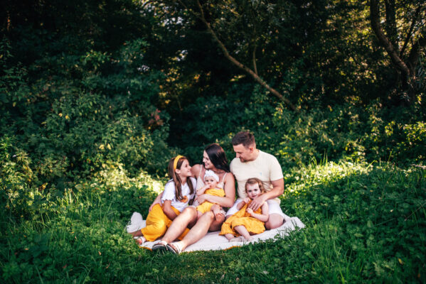 family of five in yellow cuddle on blanket in a sunlit field Essex family portrait childhood baby photographer