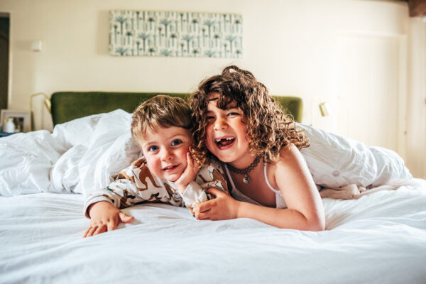 little boy and his sister cuddle on a bed at home Essex family lifestyle childhood baby photographer