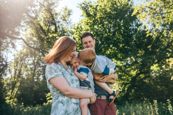 family of four stand in sunny park as big brother kisses little brother Essex family lifestyle baby childhood photographer