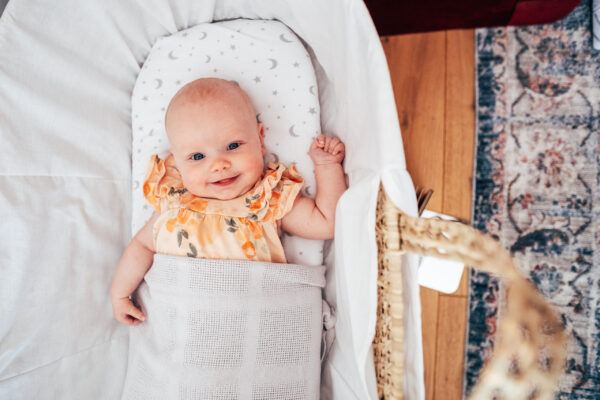 Baby girl in orange smiles up at the camera as she lays in her Moses basket Essex lifestyle family baby childhood photographer