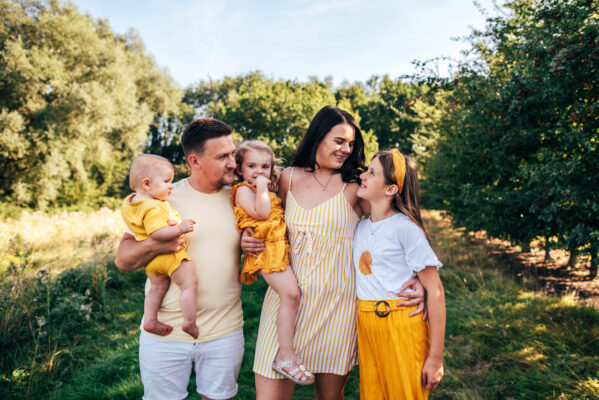 Family of five in yellow cuddle and laugh in a sunlit field Essex lifestyle family childhood photographer