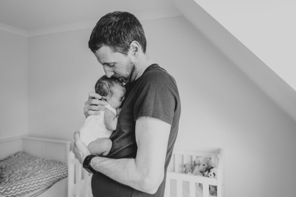 dad holds newborn son in his nursery at home Essex family lifestyle portrait baby childhood photographer