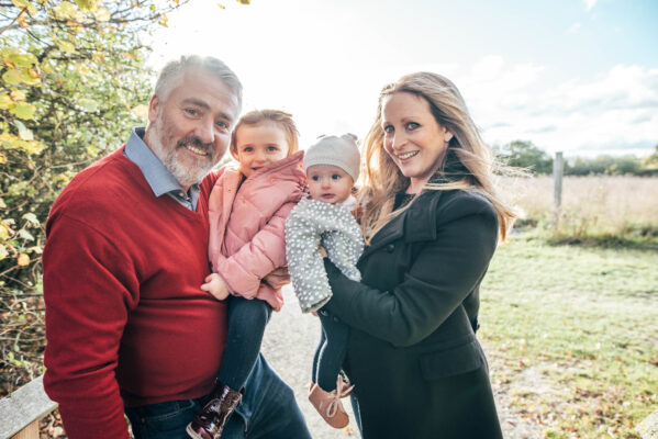 family of four smile at camera in autumn field Essex family lifestyle childhood baby photographer