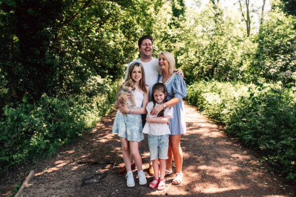 Family of four and dog laugh on sunlit path Essex family lifestyle childhood baby photographer