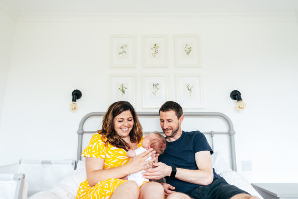 new parents cuddle their baby on their bed at home Essex portrait family newborn baby childhood photographer