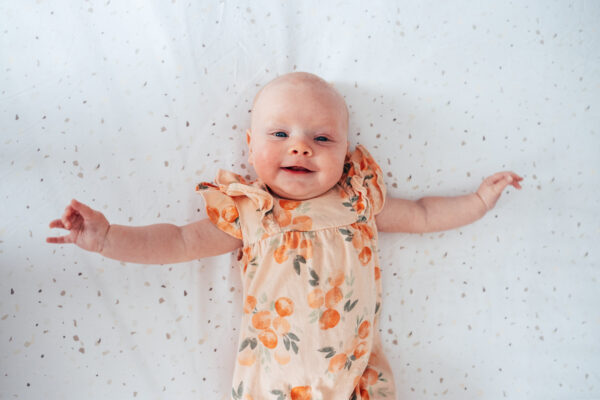 baby girl in orange romper smiles up at camera at home Essex lifestyle family baby childhood photographer