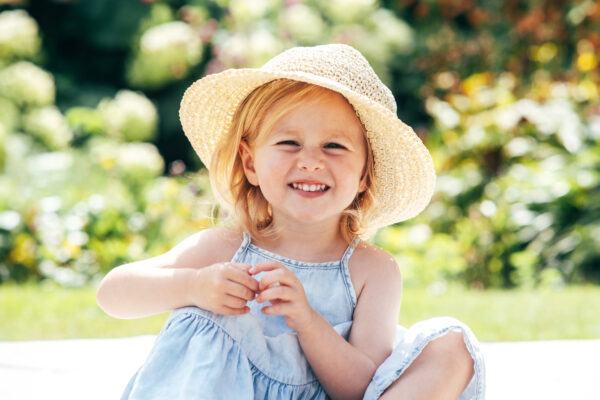 Little girl in straw hat smiles in park Essex family lifestyle baby childhood photographer