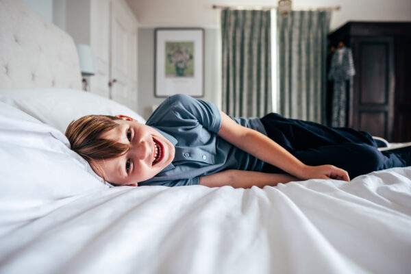 little boy laughs at camera while laying on bed at home Essex family lifestyle baby childhood photographer