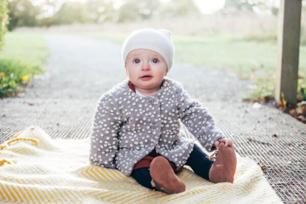 Little girl with white hat sits on blanket in autumn Essex lifestyle family baby childhood photographer