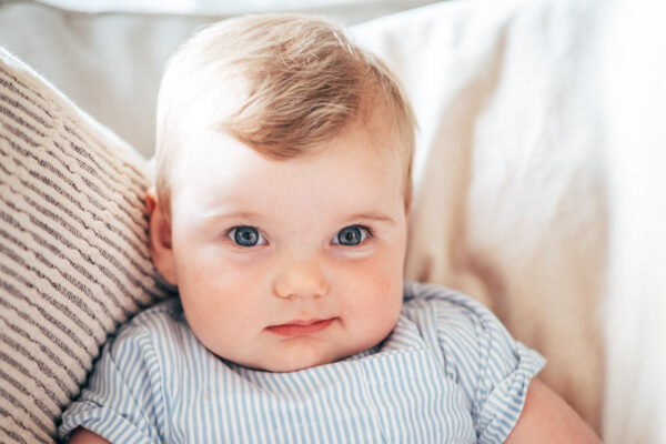 Baby girl smiles at camera as she sits on sofa at home Essex family lifestyle baby childhood photographer