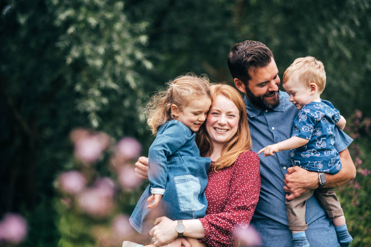 Family of four laugh and hug with purple flowers in foreground Essex family lifestyle baby childhood photographer