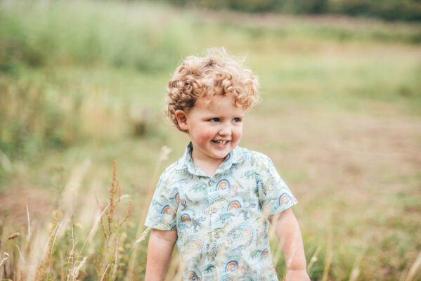 Little boy with curly hair smiles in some long grass Essex family lifestyle childhood baby photographer