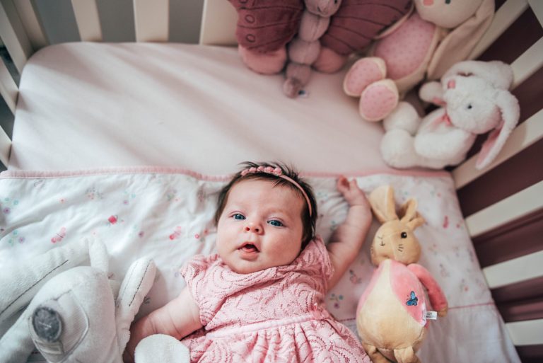 Baby girl in pink in her cot looks into camera Essex lifestyle family baby photographer