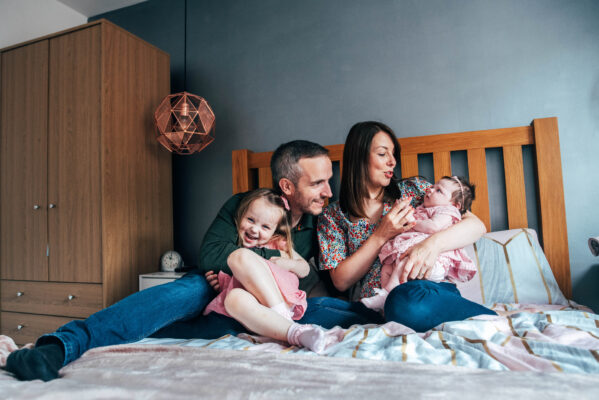 Family of four cuddle and laugh on bed Essex at home family portrait lifestyle photographer