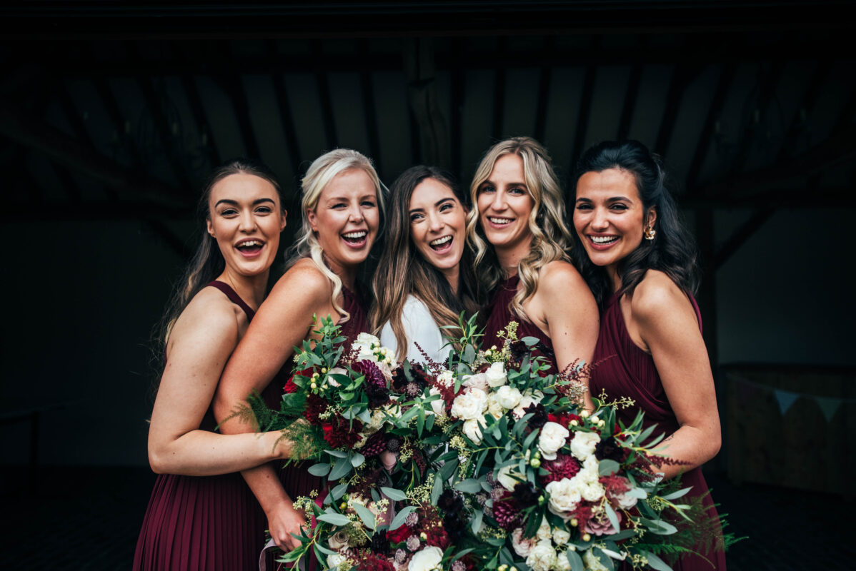 bride and bridesmaids in red laugh at Blake Hall Best Essex documentary wedding photographer