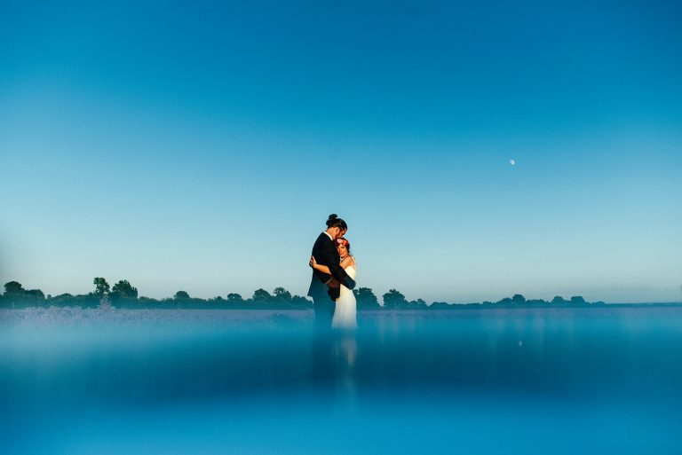 Groom in black tie hugs bride in flower crown in a field at blue hour. Houchins. Best Essex documentary wedding photographer