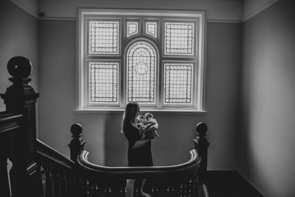 mum and newborn stand under window on stairs Essex family childhood lifestyle photographer