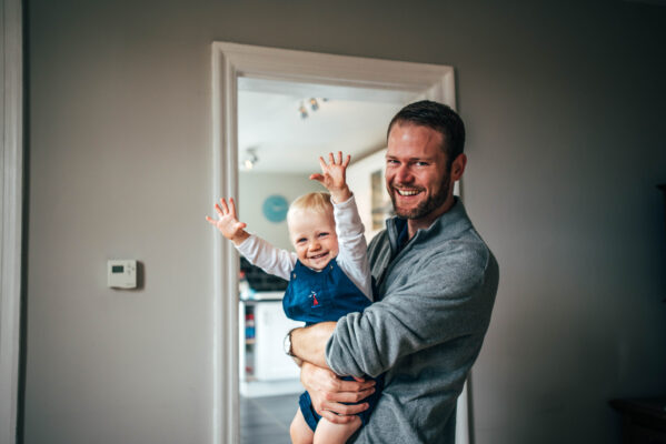 Dad holds laughing toddler son in the doorway of his kitchen Essex lifestyle family baby childhood photographer