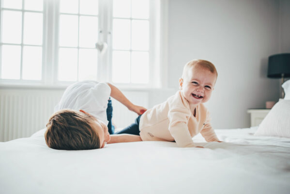 Baby girl and her brother laugh and tickle on bed Essex lifestyle family childhood baby photographer