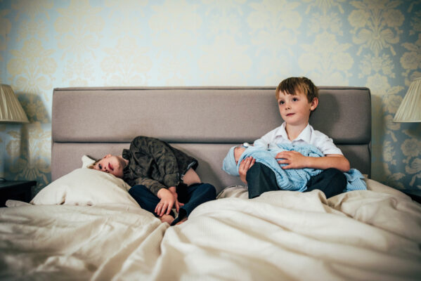 Little boy flops on bed as his big brother holds his baby brother Essex documentary lifestyle family childhood photographer