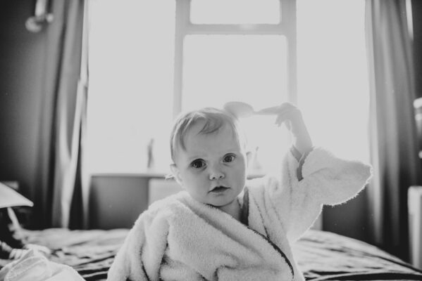 Baby girl in a towel brushes her own hair on a bed Essex family lifestyle childhood photographer