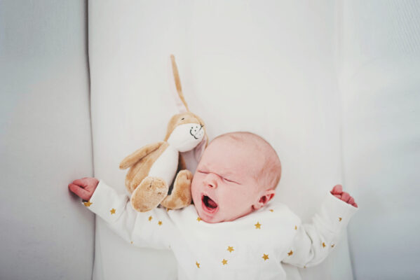 baby girl with toy rabbit yawns in crib Essex family lifestyle at home baby childhood photographer