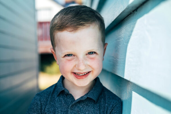 little boy laughs into camera next to blue beach hut on Mersea Island Essex family lifestyle baby childhood photographer