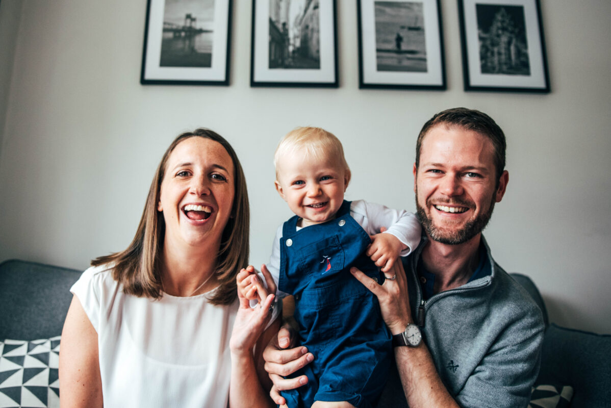 mum dad and toddler boy laugh on sofa at home lifestyle family childhood baby photographer Essex