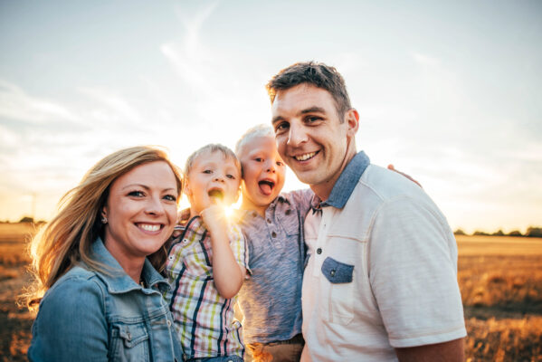 family of four laugh into camera in field at sunset Essex family lifestyle baby childhood photographer