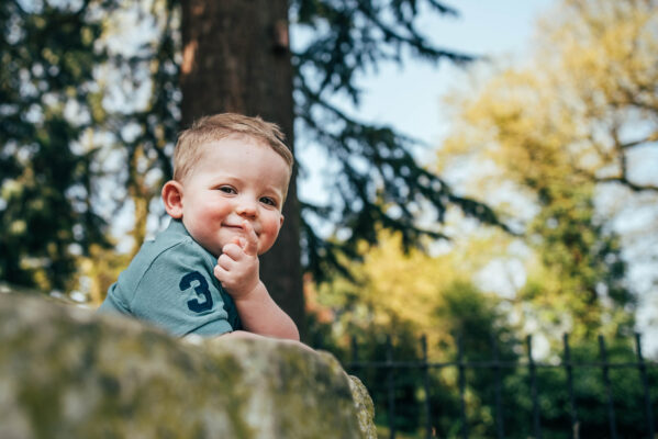 Little boy covers mouth with fingers in sunny park Essex family lifestyle baby childhood photographer