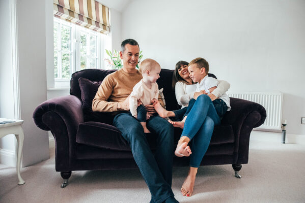 family of four laugh on a purple sofa at home family portrait baby childhood photographer Essex