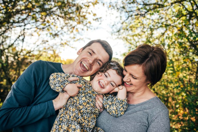 mum and dad cuddle little girl in autumn dress in park Essex family lifestyle baby childhood photographer