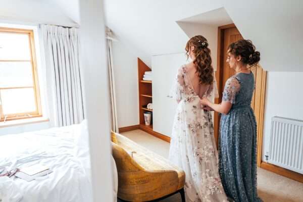 Bridesmaid in blue helps bride into her House of Savin gown for Captains Wood Barn wedding