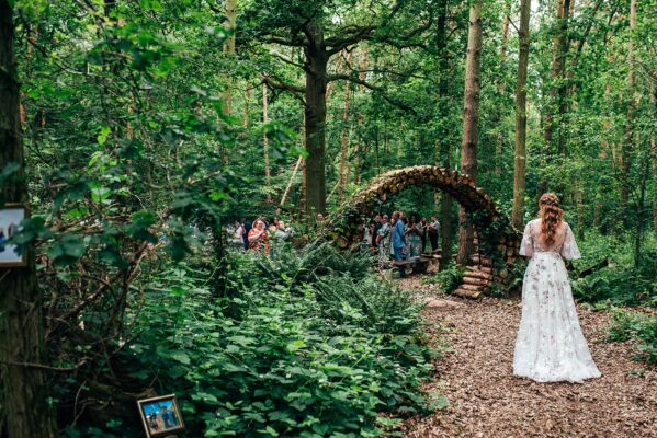 Bride walk towards log arch to her wedding ceremony as guests look on at Captains Wood Barn