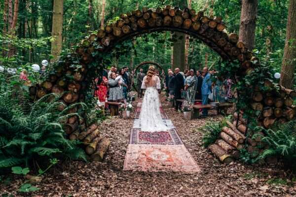 Bride walks down aisle towards groom in woodland wedding ceremony at Captains Wood Barn