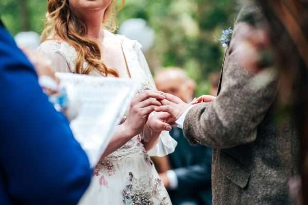 Bride places ring on Groom's finger during woodland ceremony at Captains Wood Barn